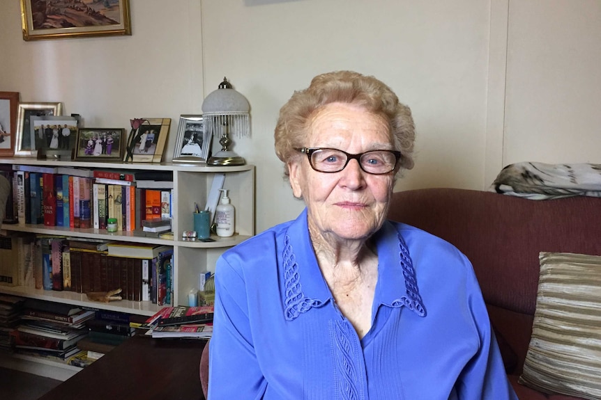 Beryl Keenan from Broken Hill sitting on her lounge chair with a bookshelf in the background.