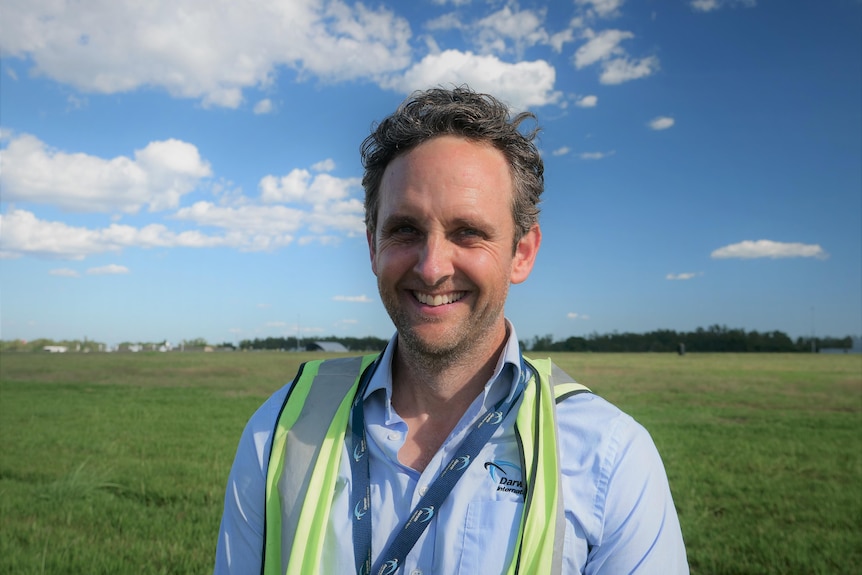 Headshot of man in hi-viz vest with green grass behind and flat horizon.