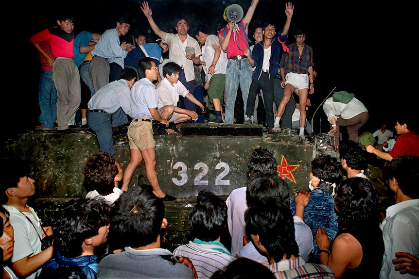 A group of chinese people climb on a tank and look angry.