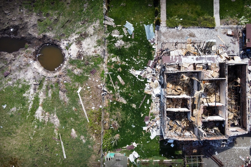 A drone shot of a blasted house, with a huge crater in the yard where a rocket landed 