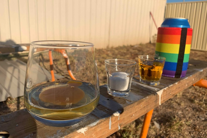 A glass with a raw egg in it, a shot of sugar, shot of alcohol, and a beer rest on a sawhorse.
