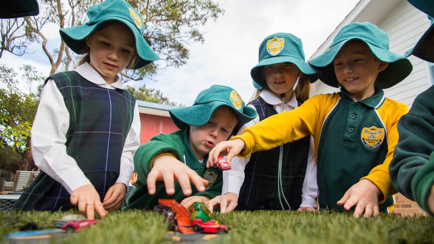 A group of children stand in a group playing with toy cars.