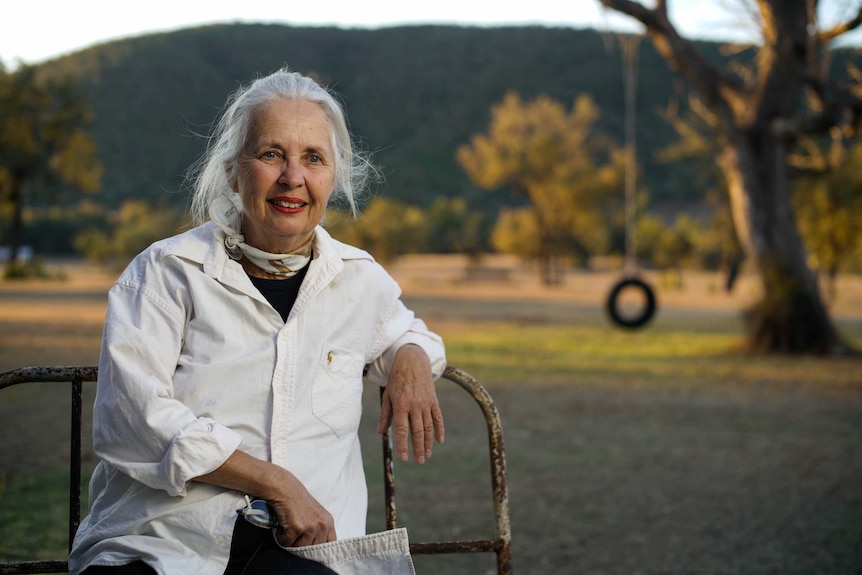 Mingoola resident Julia Harpham sits on a bench in front of an old tree with a tyre swing