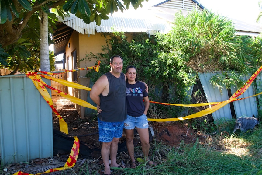 Couple stand infront of their buckled fence in backyard