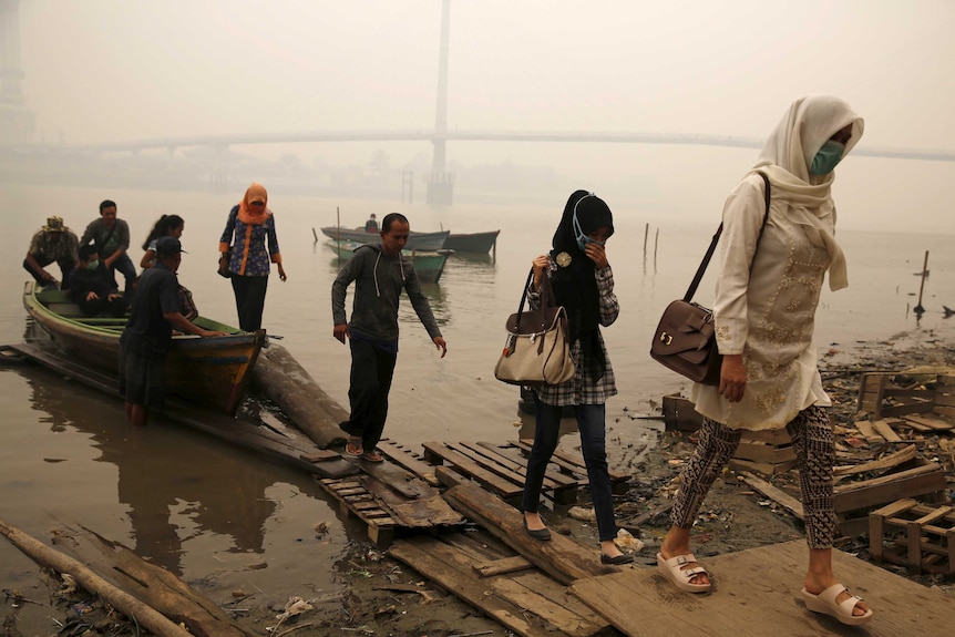 Workers disembark a boat on a riverbank, shrouded in haze.