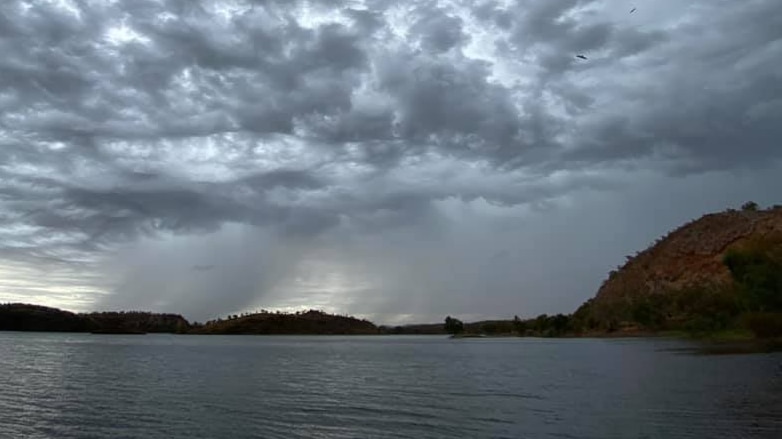 A photo of a large lake - the sky is covered in dark clouds with rain falling in the distance.