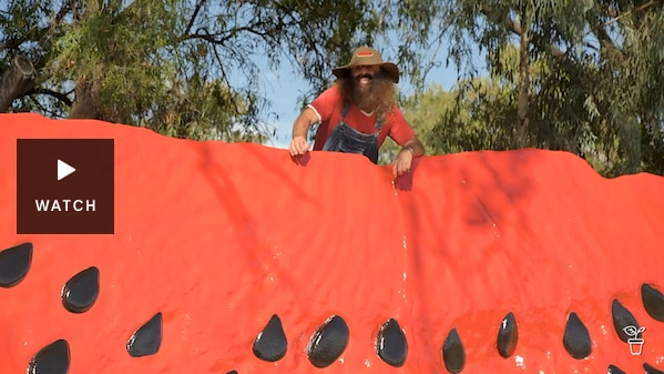 Costa standing behind a large watermelon sculpture. Has Video