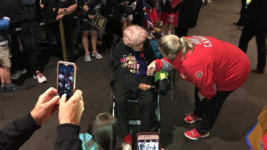 people taking photos of elderly woman in a wheelchair in middle of crowd