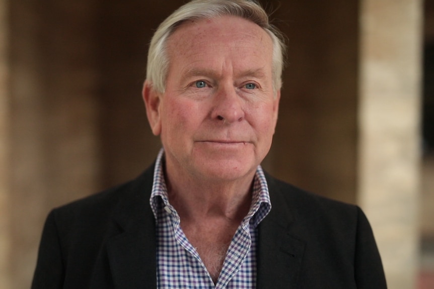 Colin Barnett wears a collared shirt and blazer pictured in front of limestone pillars