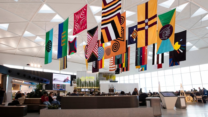 28 large flags by artist Archie Moore hanging from the ceiling of T1 International terminal.