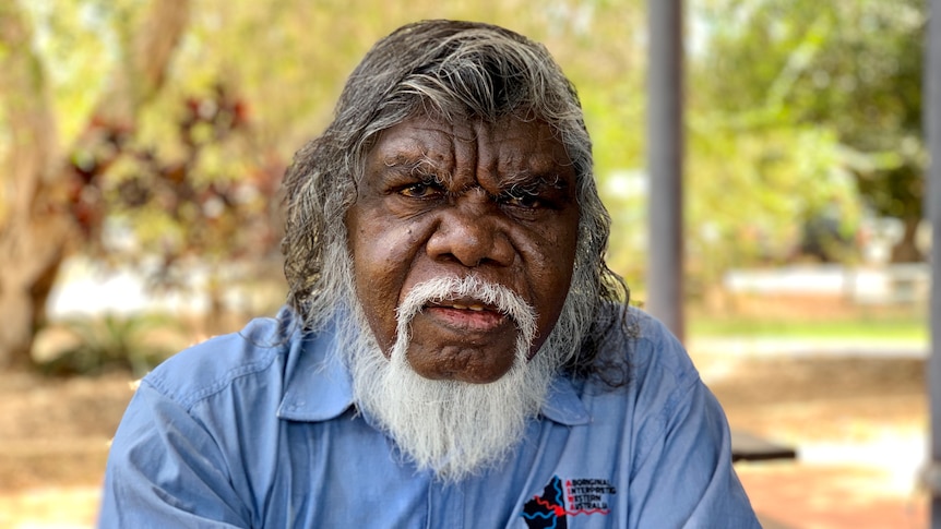 An Aboriginal man with a white beard stares at the camera