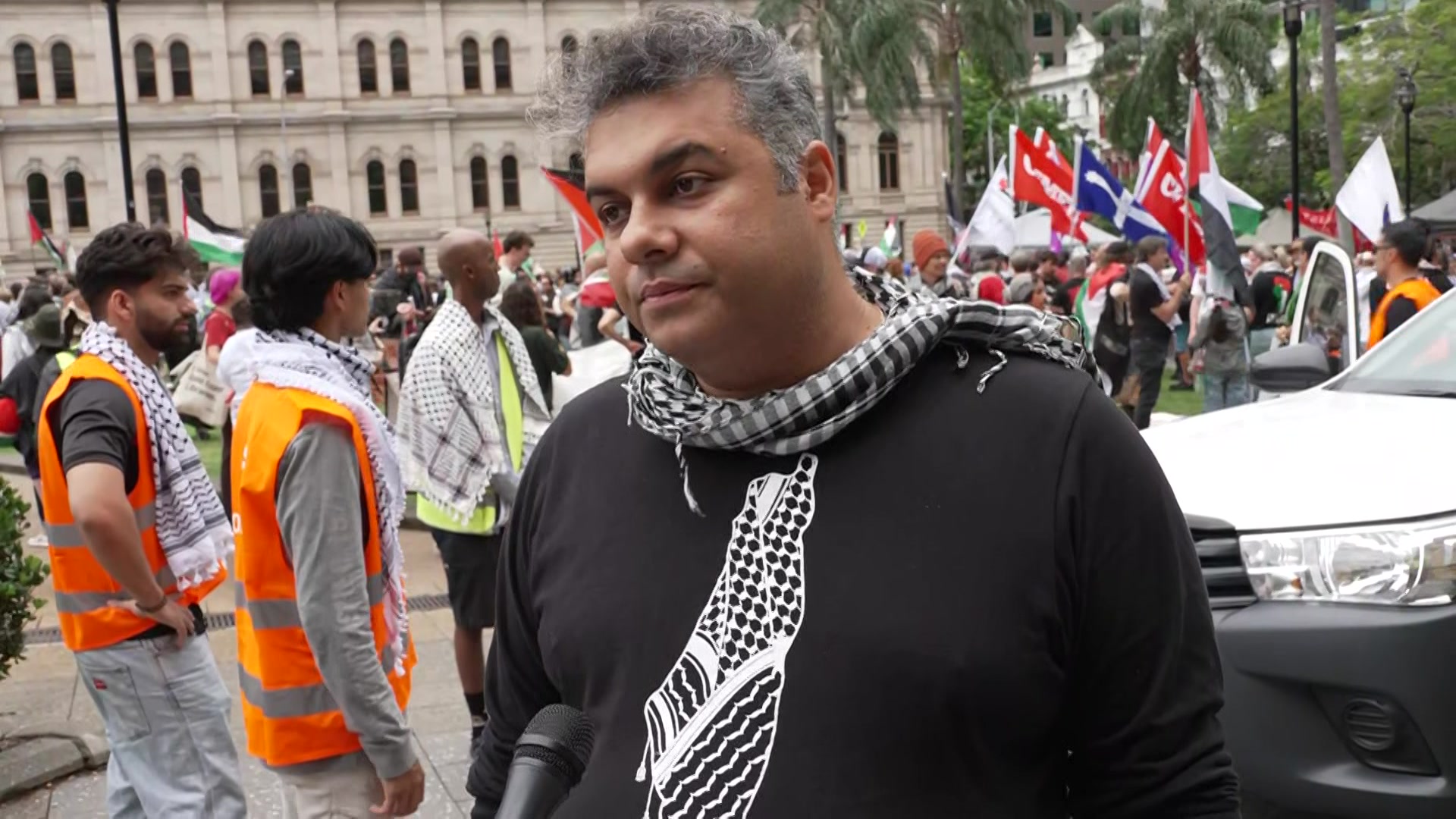 A man wearing a chequered scarf standing in front of a flag-waving crowd. 