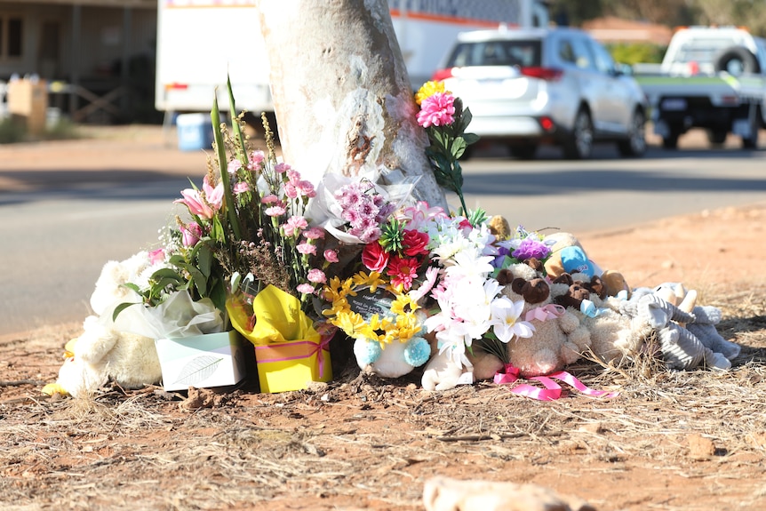 Flowers, teddy bears and cards sit propped against a tree near the scene of a tragic house fire in Port Hedland. 