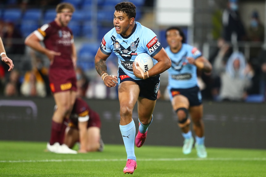 Latrell Mitchell runs with the ball under his arm and his mouth open