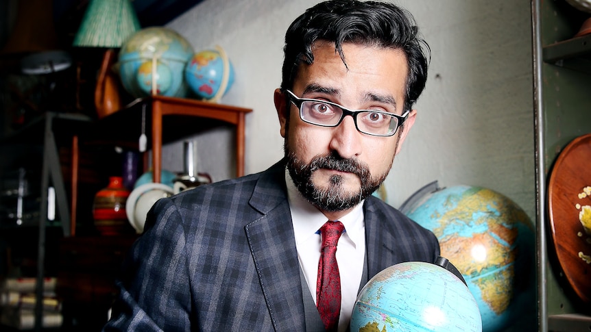 Sami Shah dressed in a suit holding a globe of the world.