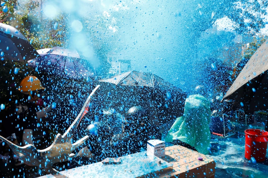 Hong Kong protesters are sprayed with blue water from a cannon.