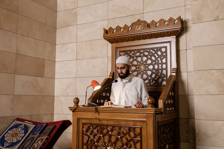 An imam stands on a minbar in a mosque.