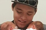 Sterling Free holds two babies while smiling and looking at them.