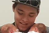 Sterling Free holds two babies while smiling and looking at them.