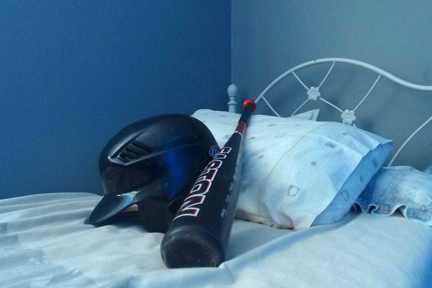 Baseball bat and helmet on bed.