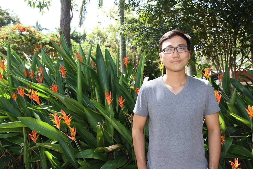 Vietnamese student Zac Bai stands in a tropical setting with strelizia flowers in the background.