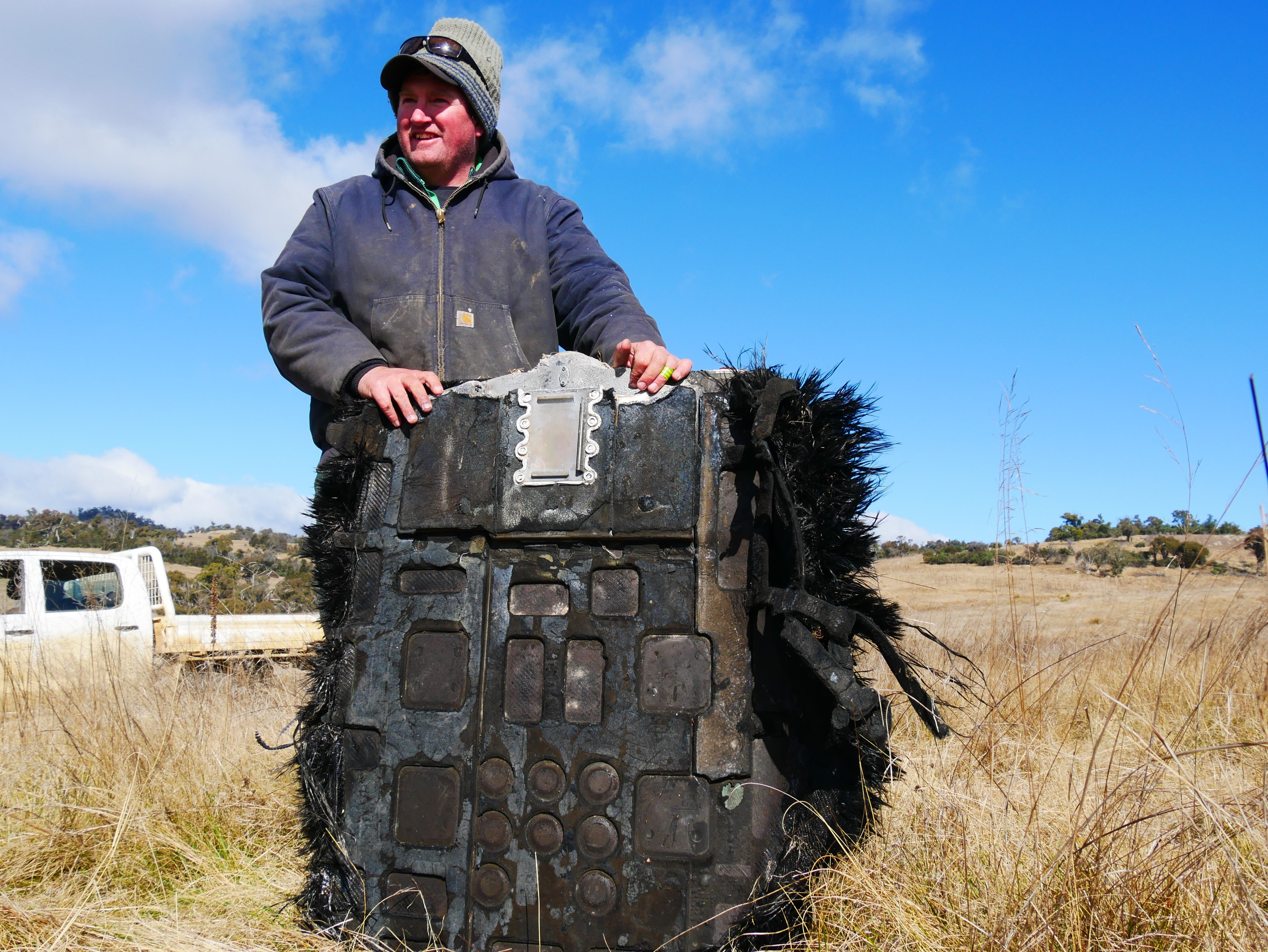 a man stands in a paddock holding space junk