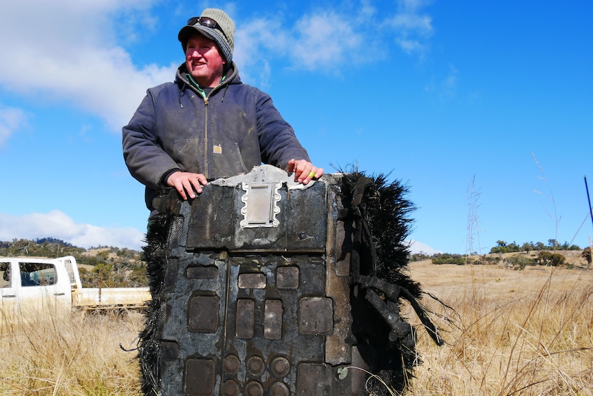 A man holds a piece of debris in a paddock