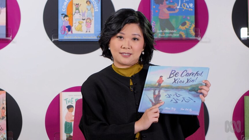 Teacher FangNi Zhou holds up story book, Be Careful, Xiao Xing!