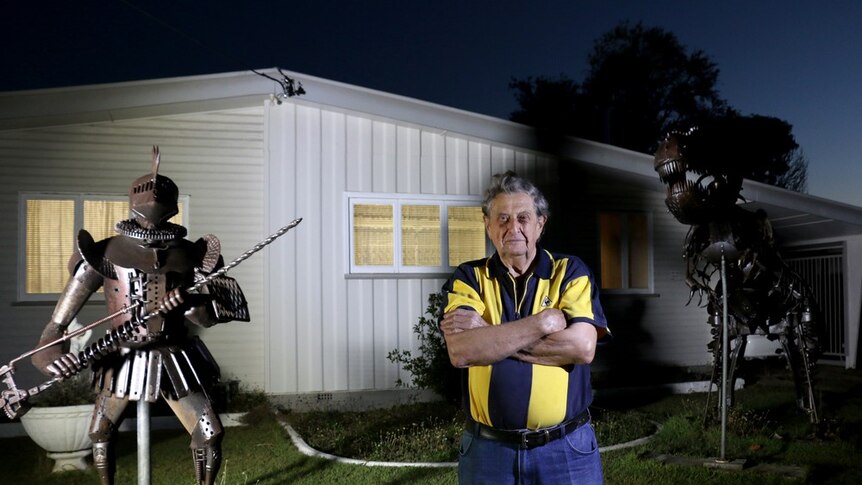 A man stands at night time in his front yard in front of two large recycled metal sculptures