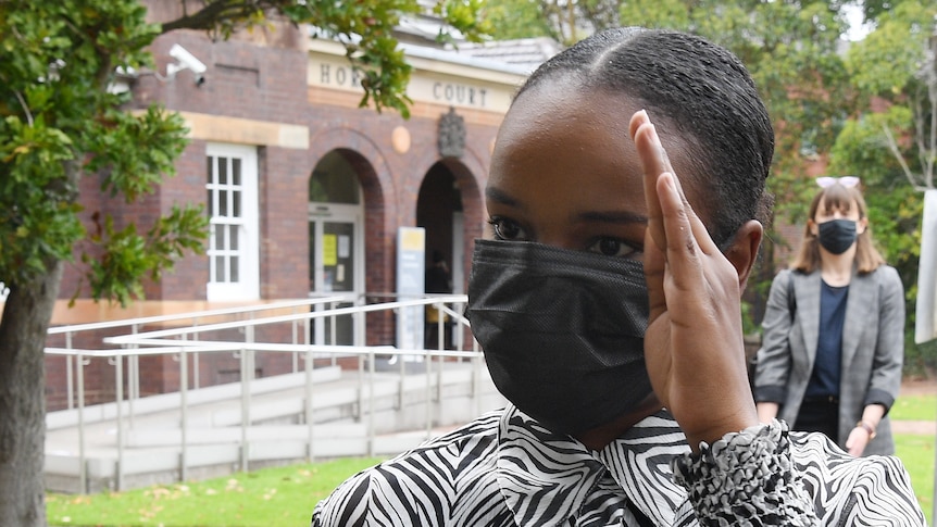 A woman wearing a mask holds her hand up 