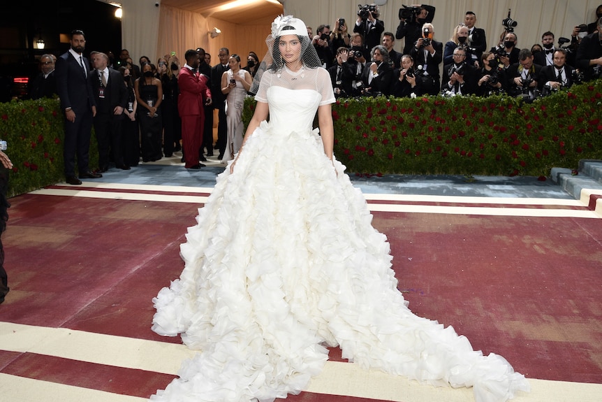 Kylie Jenner wearing a big puffy-skirted white gown with a whit baseball cap with the fishnet veil