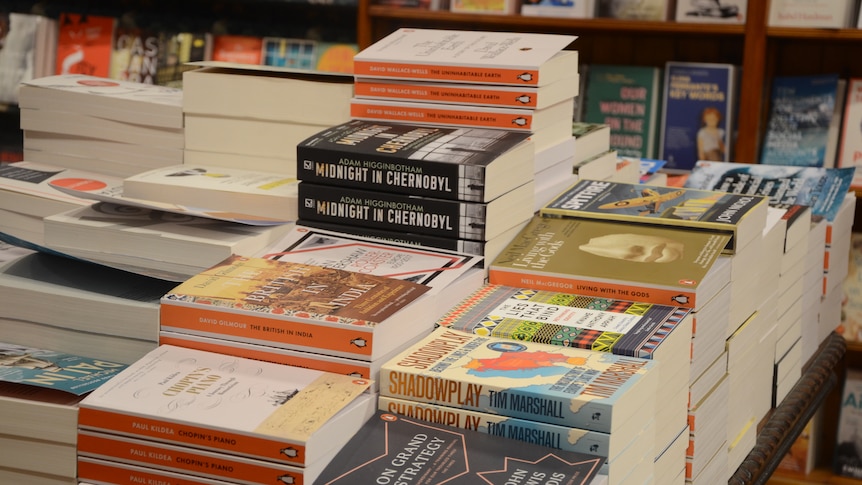 Multiple stacks of books cover a table. 