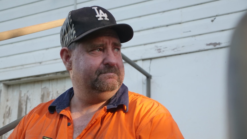 man wearing high-vis work shirt and base ball cap, looking away from the camera with glassy eyes