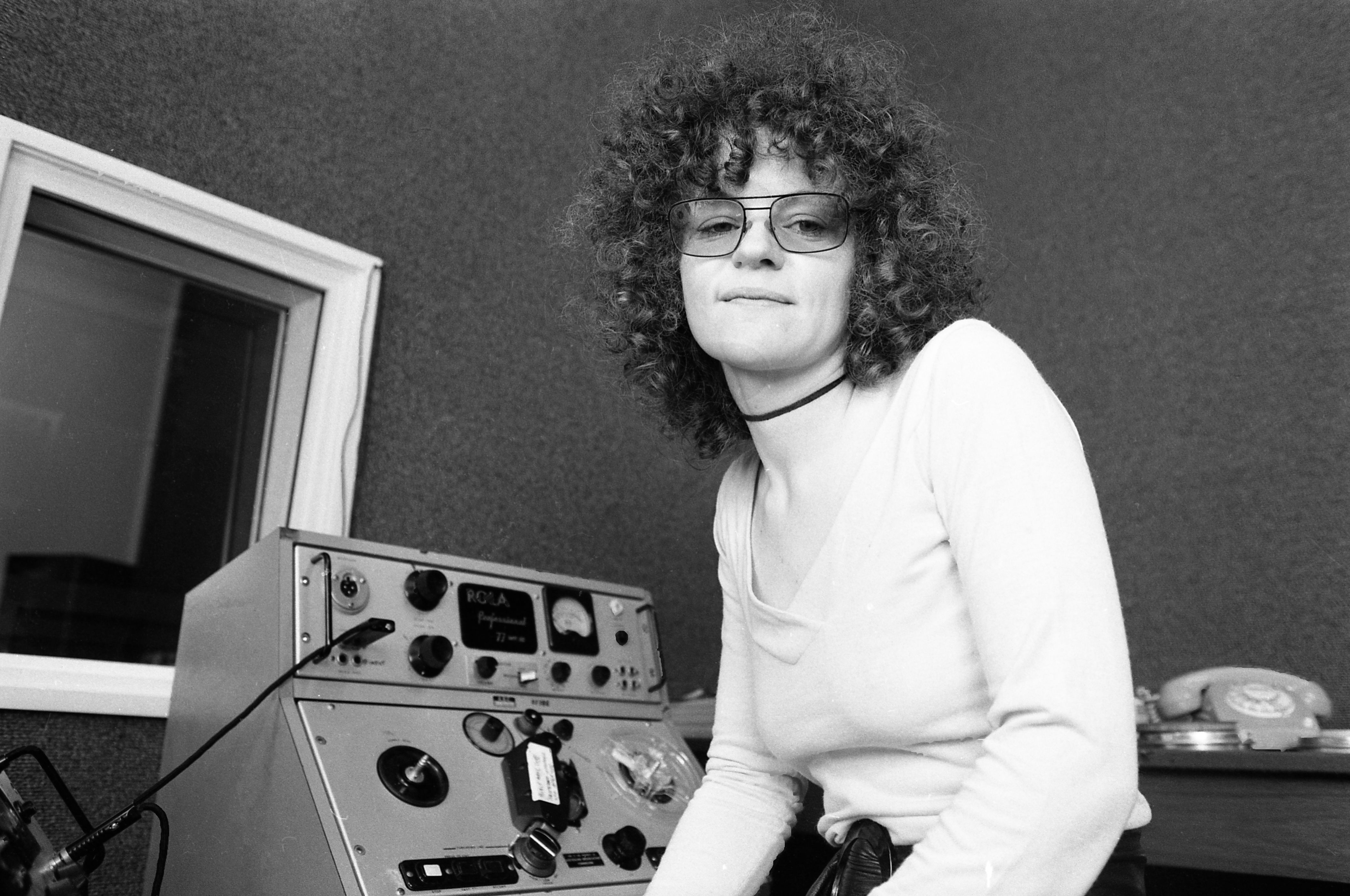 black and white photo of woman with curly hair and light sunglasses in a radio studio 