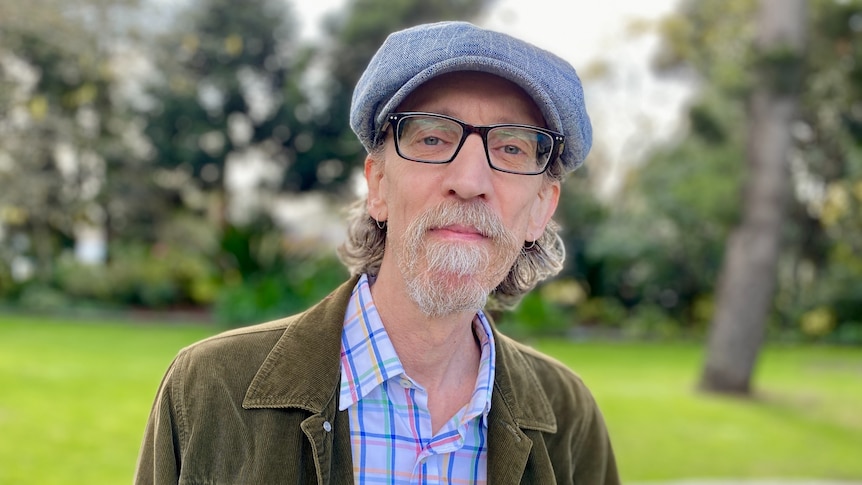 a man wearing glasses and a hat. there are trees behind him.