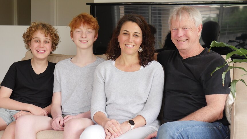 A smiling family portrait shows two young boys with 40-something parents sitting on a couch.