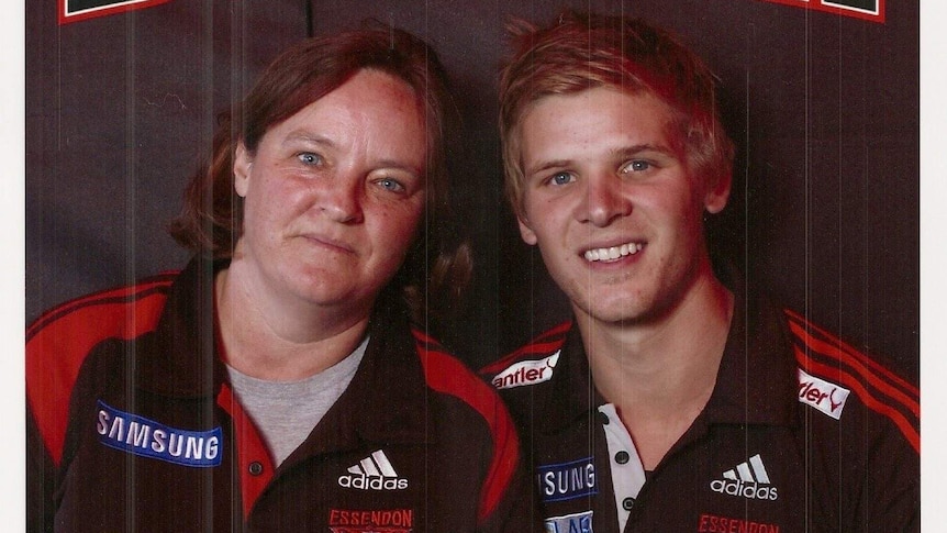 An Essendon fan smiles at the camera, as a young Bombers player stands next to her in a team top.