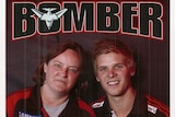 An Essendon fan smiles at the camera, as a young Bombers player stands next to her in a team top.