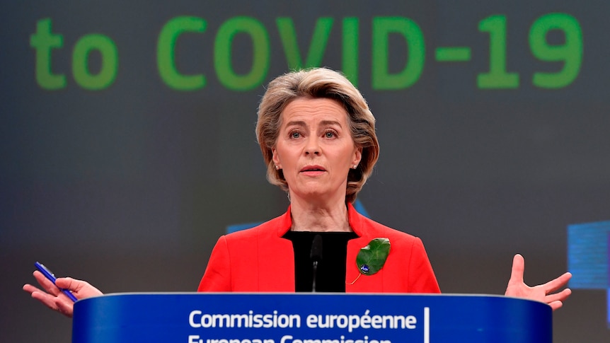 Ursula von der Leyen stands at a podium with her hands outstretched. A screen behind her reads "COVID-19".