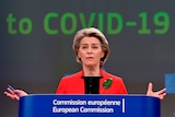 Ursula von der Leyen stands at a podium with her hands outstretched. A screen behind her reads "COVID-19".