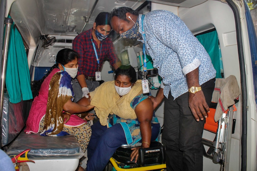 A woman is assisted by others to get down from an ambulance at hospital