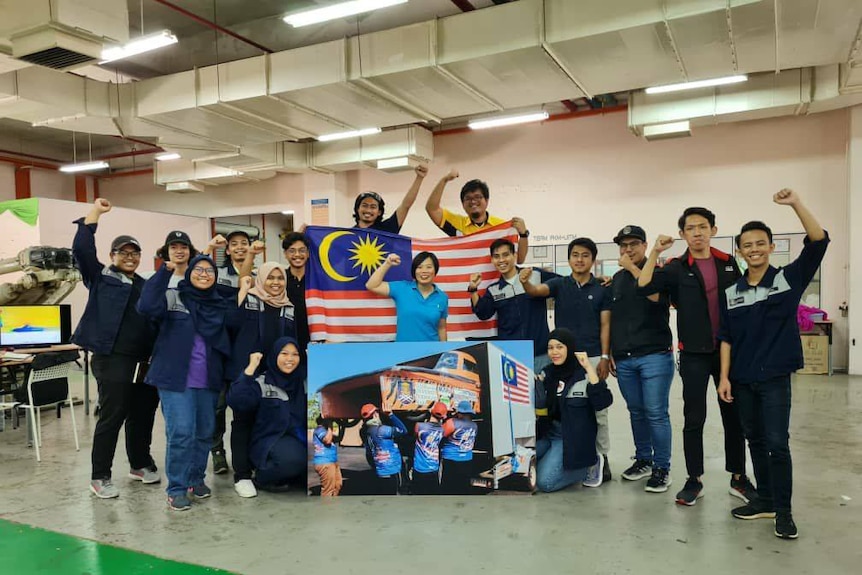 A team photo indoors holding Malaysian flags.