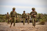A group of Australian Army soldiers in full combat gear walk across an open field during an infantry exercise in Australia