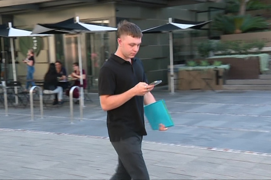 A man in a polo shirt walks along the street while looking at a phone. 