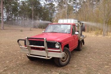 A red ute with a water tank and hoses on the back.