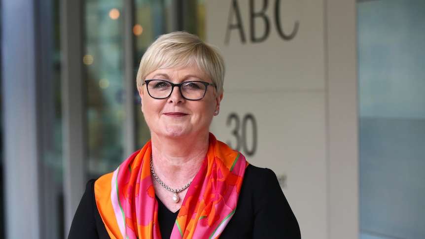 A happy smiling woman wearing glasses and a brightly coloured scarf over a dark blouse. 