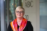 A happy smiling woman wearing glasses and a brightly coloured scarf over a dark blouse. 