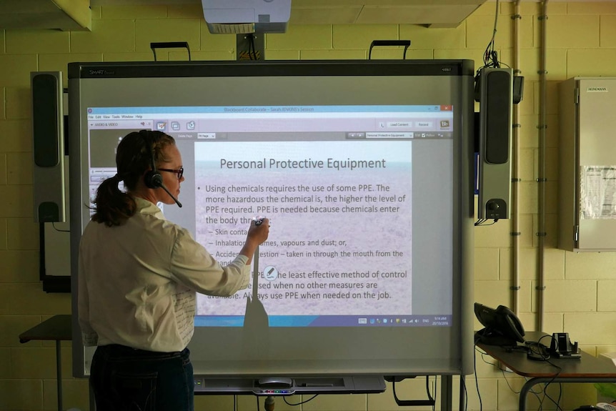 A woman teacher writes on a whiteboard in a classroom for distance education