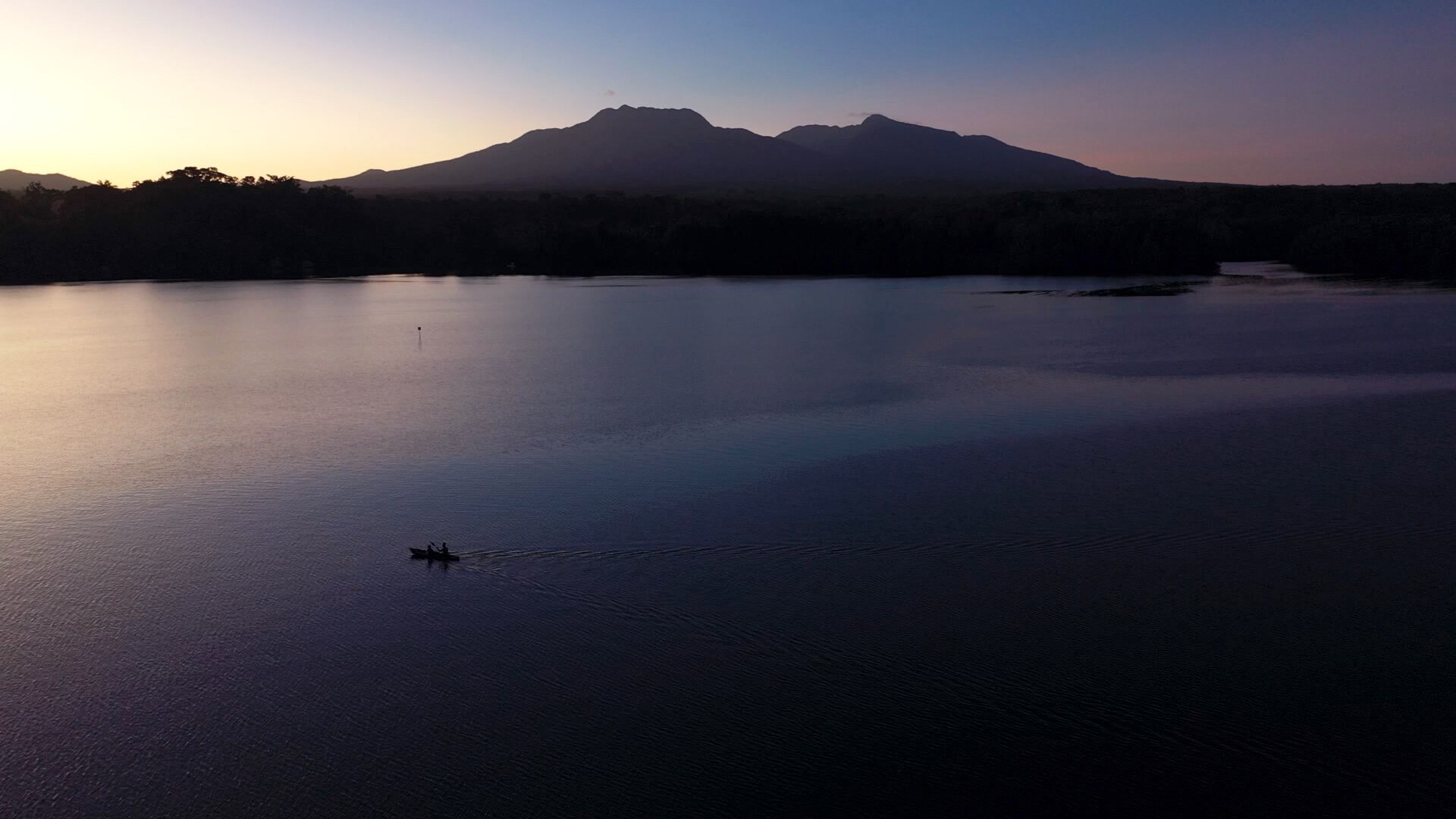 An aerial photo of the island in the distance. A small boat can be seen in the foreground in the ocean.