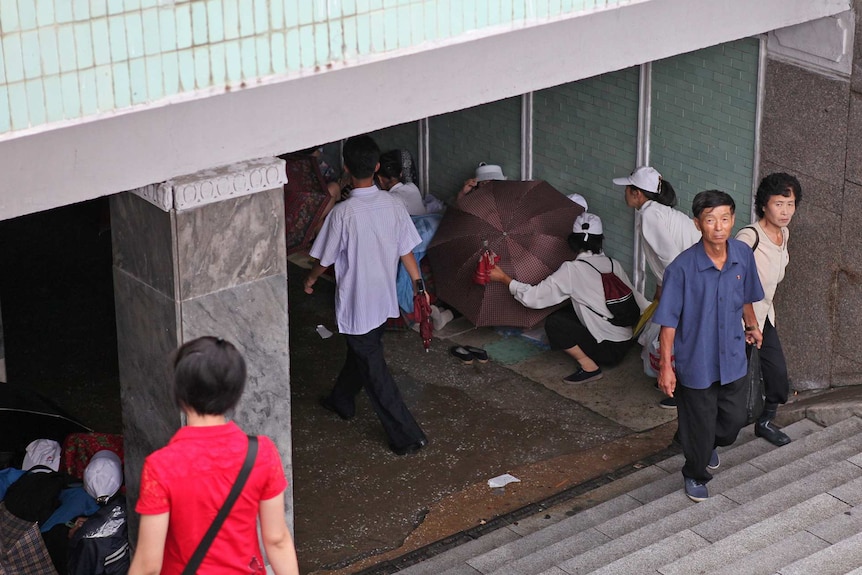 Looking down into the entrance of an underpass people walk up steps, and people shield others with umbrellas.